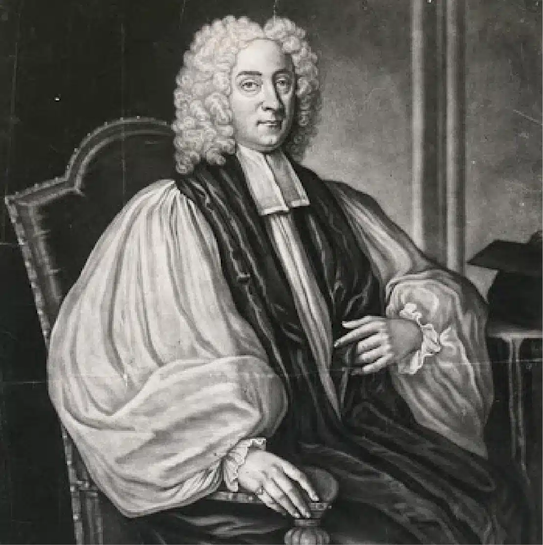 A black-and-white portrait of a person wearing an 18th-century clerical outfit, including a white wig, a dark robe, and a white ruffled shirt. They are seated on an ornate chair, with a hand resting on their lap. A book is partially visible to their side.